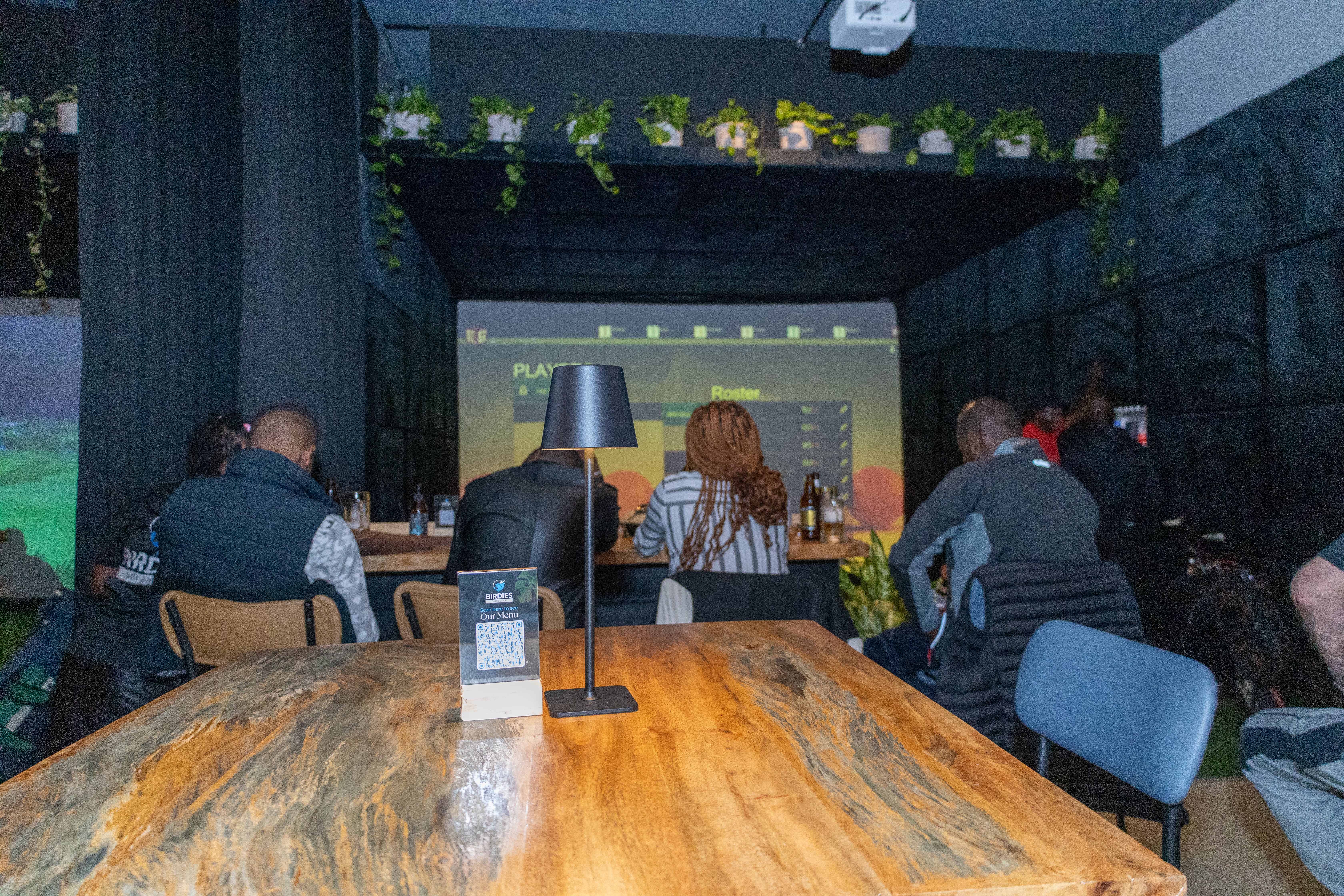 View from a table of patrons in a dimly lit indoor golf simulator bar